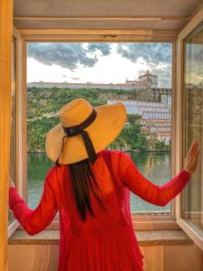a woman in a hat looking out a window at Red House By The River in Porto