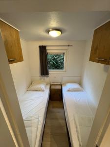 twee bedden in een kleine kamer met een raam bij Chalet Hoenderloo in Hoenderloo