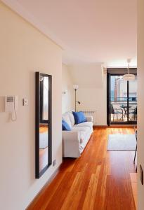 a living room with a white couch and a wooden floor at Ático con terraza, vistas al mar y parking en playa de S Lorenzo in Gijón