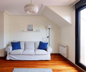 - un canapé blanc avec des oreillers bleus dans le salon dans l'établissement Ático con terraza, vistas al mar y parking en playa de S Lorenzo, à Gijón