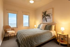 a bedroom with a bed and a chair and two windows at Sol Living Beach House in Hardwicke Bay