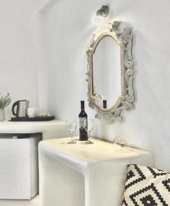 un tavolo bianco con specchio, bottiglia e bicchieri di Villa Maina a Kamari