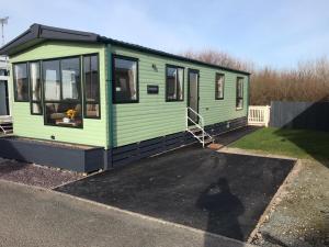 a green tiny house sitting in a parking lot at Tranquility - Static Caravan Lune Park on Parkdean Ocean Edge Resort in Heysham
