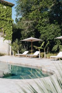 2 sillas y sombrilla junto a la piscina en Le Château Réal, en Saint-Seurin-de-Cadourne