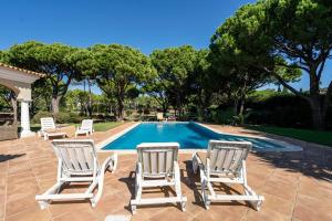 two lawn chairs and a swimming pool with trees at Casa Atlantico in Quinta do Lago
