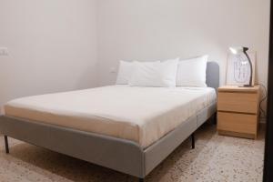 1 cama con sábanas blancas y mesita de noche con lámpara en Retrophilia Home, en Nápoles