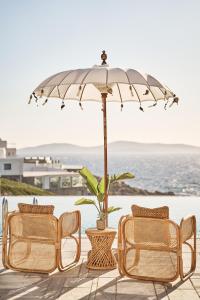 a patio with chairs and an umbrella and the ocean at Ubud Mykonos in Agios Ioannis Mykonos