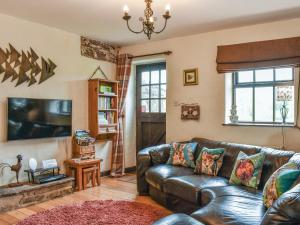 a living room with a leather couch and a tv at Stoney End Cottage in Askrigg