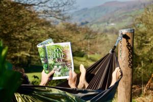 uma pessoa deitada numa rede a ler um livro em Bluebell huts em Abergavenny