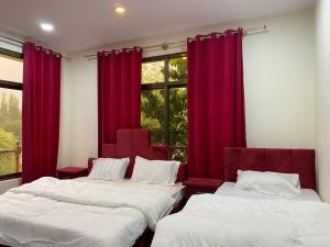 two beds in a room with red curtains and a window at Kamals Lodge in Skardu