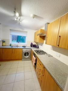 eine Küche mit Holzschränken, einer Spüle und einem Geschirrspüler in der Unterkunft Cozy Nights SVP Detached House in Nitshill