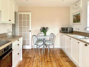a kitchen with white cabinets and a table with chairs at Foresters Cottage in Kildary
