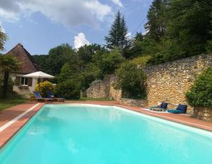 une grande piscine avec des chaises et un mur en pierre dans l'établissement Le Baron Perché, à Saint-Cyprien
