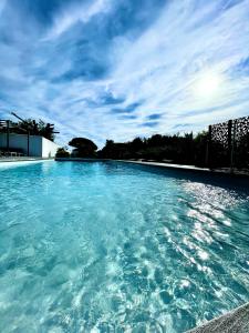duży basen z niebieską wodą z pochmurnym niebem w obiekcie Le 36 Maison d'hôtes Piscine & Spa w mieście La Flotte