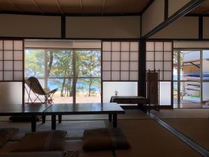 a room with a table and a chair and windows at 奈多みどり荘 Nada Beach House in Kitsuki