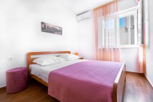 a bedroom with a bed with a purple blanket and a window at Apartmani Roko in Baška Voda