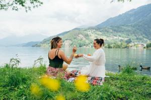 deux femmes assises sur l'herbe près d'un lac dans l'établissement Eco Lodges Millstätter See, à Döbriach