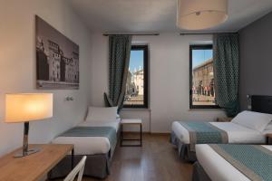 a room with two beds and a table and two windows at Hotel dei Gonzaga in Mantova