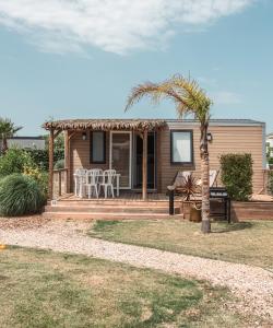 a small house with a patio and a palm tree at Camping Le Calypso 5 étoiles in Torreilles