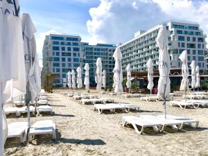 a beach with white umbrellas and chairs and buildings at Veli Apartments 348 Infinity in Mamaia Sat/Năvodari