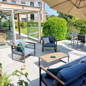 un patio con sillas, mesas y una sombrilla en LES JACQUEMARTS NORMANDS Maison d'hôtes - Guesthouse, en Belmesnil