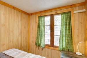 1 dormitorio con paredes de madera y una ventana con cortinas verdes en Lakefront Cabin with Deck, Games, and Views!, 