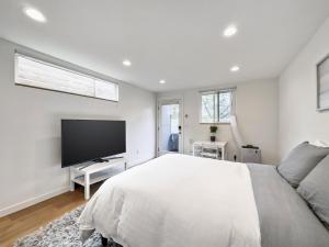 a white bedroom with a large bed and a flat screen tv at Modern apartment near light rail in Seattle