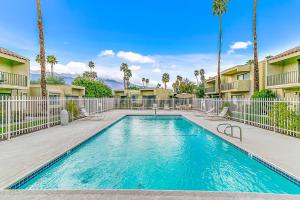 a swimming pool with palm trees and buildings at Villa De Las Flores in Palm Springs