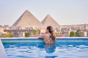 New Pyramid Front Hotel في القاهرة: امرأة في مسبح مع الاهرامات في الخلفية
