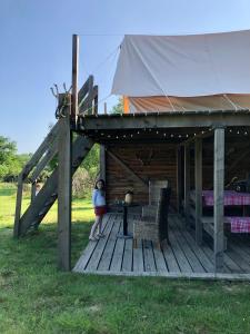 una chica parada en una terraza de madera con una tienda de campaña en Tente bivouac Élevage Girbal en La Chapelotte