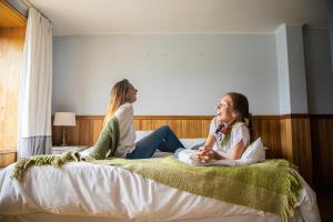 Duas raparigas estão sentadas numa cama. em Hotel Bellavista em Puerto Varas