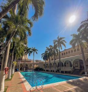 a swimming pool with palm trees in front of a building at Hotel El Prado in Barranquilla