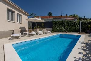 a swimming pool with chairs and an umbrella next to a house at Villa KaTess with heated pool in Split