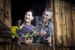Un uomo e una donna che guardano fuori da una finestra con dei fiori di Alpengasthof Karalm a Rauris