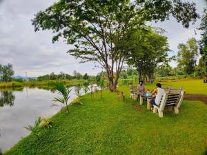 two people sitting on benches next to a lake at Canal Side Safari Resort in Udawalawe