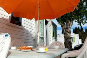 einen Tisch mit orangefarbenem Regenschirm und Essen drauf in der Unterkunft Mobilhome Le repaire du soleil in Sigean