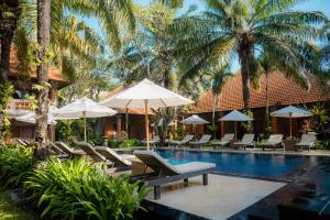 a resort pool with lounge chairs and umbrellas at Griya Santrian a Beach Resort in Sanur