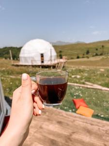 una persona che tiene una tazza di caffè con una yurta sullo sfondo di Glamping Park a Khndzorut