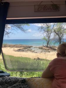 Una mujer mirando por una ventana en una playa en Oahu Camper Adventures en Kailua