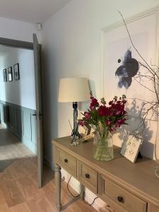 a vase of flowers on a table with a lamp at Shakespeare’s Nest in Prescot