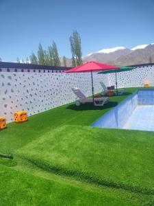 a swimming pool with a red umbrella and grass at The Royal Maryul Banquet Hall , Restaurant & Resort - Leh in Stak
