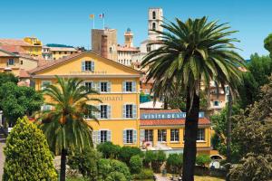 a yellow building with palm trees in a city at Studio Pampa - Centre historique - Climatisation - WiFi in Grasse