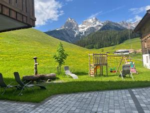 un patio con sillas y un parque infantil con montañas al fondo en Appartement zur schlafenden Jungfrau, en Hinterthal