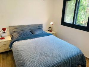 a bedroom with a bed with a blue comforter and two windows at חצר ברמה in Sha'al