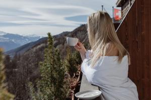 a woman holding a cup of coffee on a balcony at Boutique Hotel Panorama in Crans-Montana