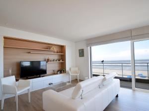 een woonkamer met een witte bank en een televisie bij Golf 0301 apartment with modern kitchen by the sea in De Haan