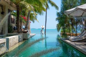 a man standing in a swimming pool next to the ocean at ODYSSEY - Luxury Beachfront Mansion - in Koh Samui