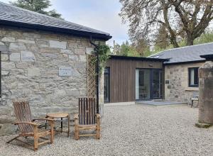 two chairs and a table in front of a stone building at Birchwood Bothy in Pitlochry