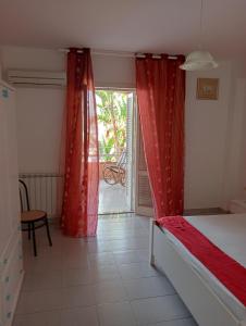 una camera da letto con letto con tende rosse e patio di trilocale "Alicudi" in Portorosa a Furnari
