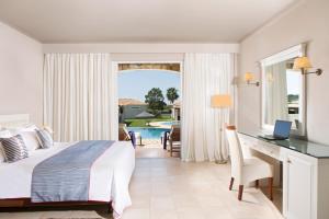 sypialnia z łóżkiem i biurkiem oraz basen w obiekcie Olympia Golden Beach Resort & Spa w mieście Kyllini